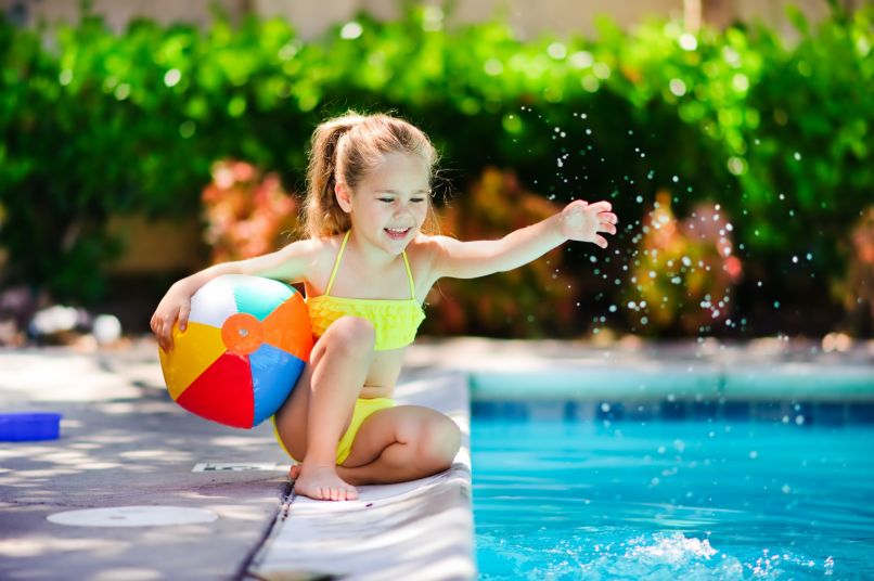 Kind mit Wasserball am Beckenrand